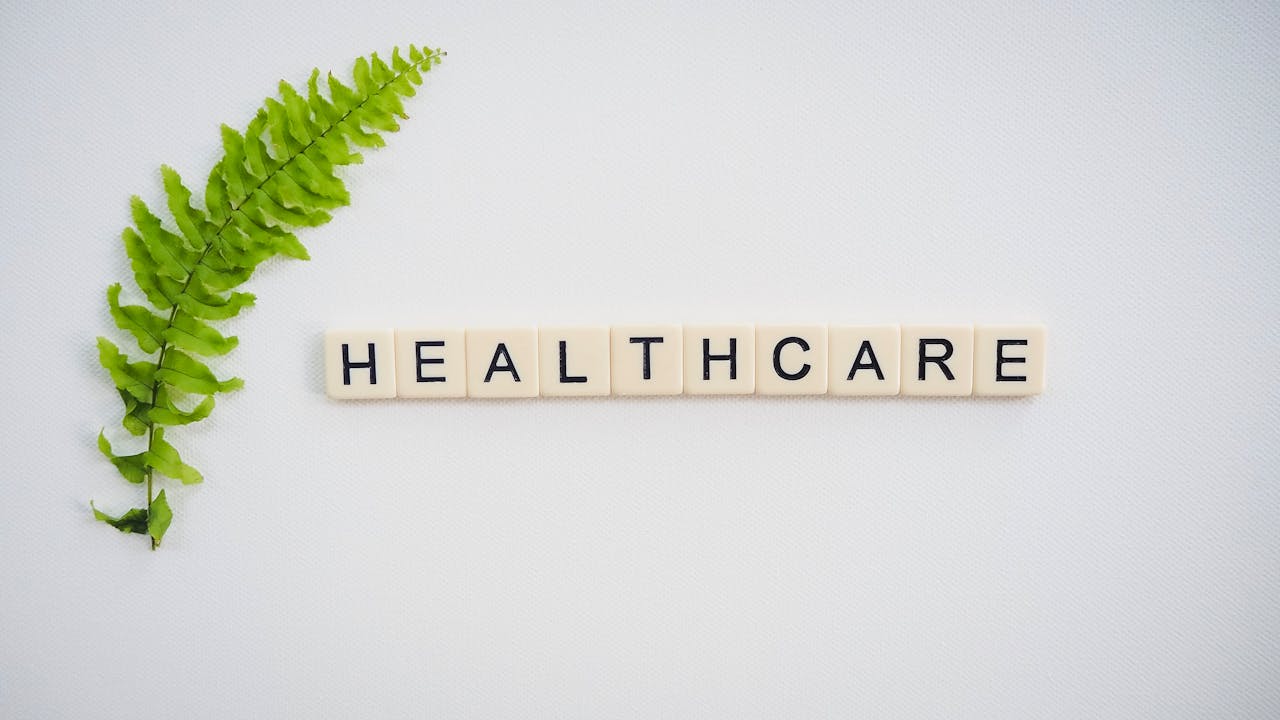 home-hero Healthcare word spelled with Scrabble tiles next to a green fern leaf on a white background.